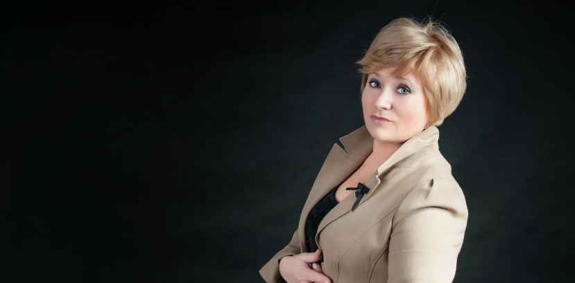 kobieta w marynarce obrócona bokiem, patrzy na wprost, dłonią splecione na brzuchu