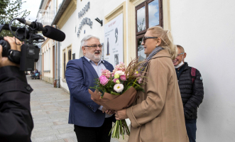 Kobieta podaje rękę mężczyźnie, a w drugiej trzyma bukiet kwiatów.