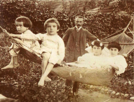 Dwójka dzieci, dwie kobiety siedzą na hamaku, a mężczyzna z wąsem stoi obok nich.
