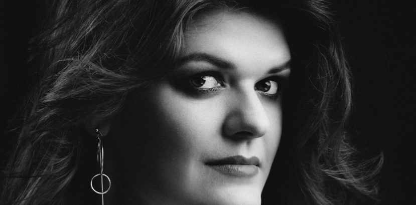 popiersie młodej uśmiechniętej kobiety patrzącej na wprost, włosy długie falowane swobodnie opadają na ramiona