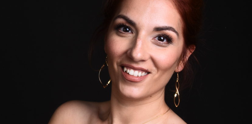 młoda uśmiechnięta kobieta patrzy na wprost, długie włosy rozpuszczone zebrane w okolicach skroni podtrzymuje dłońmi