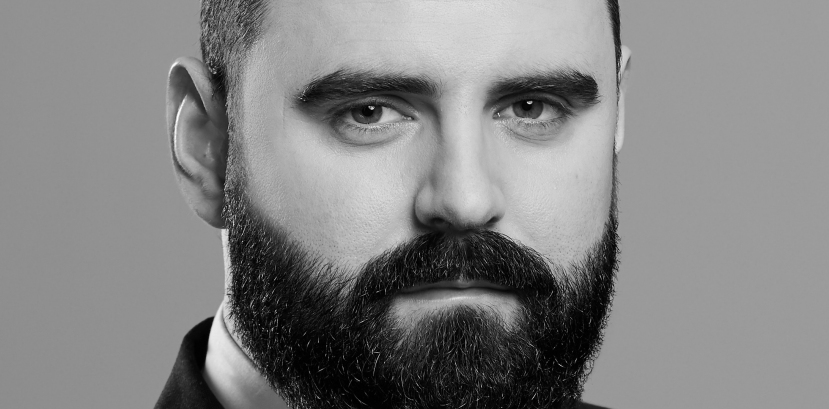 popiersie młodego mężczyzny w garniturze i krawacie, patrzącego na wporst