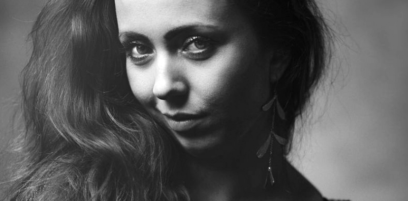 młoda kobieta w rozpuszczonych włosach zgarniętych przed lewe ramię patrzy na wprost, głowa lekko pochylona