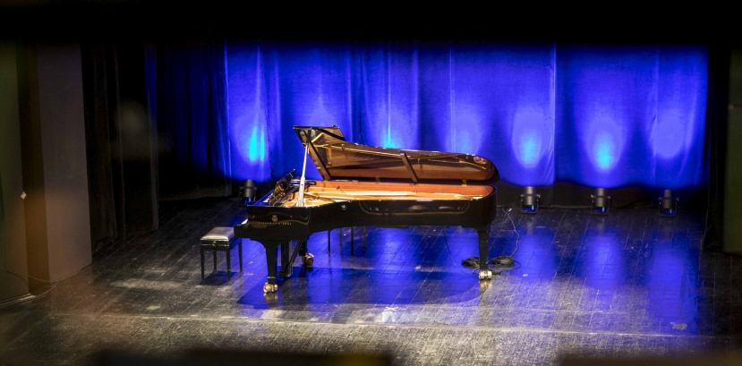 fortepian stojący na scenie, podświetlony niebieskim światłem