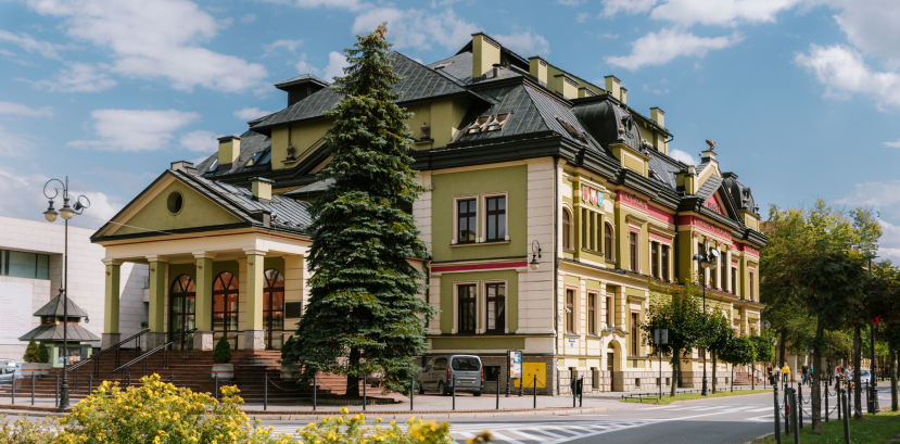 zabytkowy budynek oświetlony promieniami słonecznymi, na pierwszym planie kwitnące na żółto krzewy