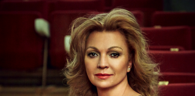 kobieta w sukni siedzi w sali koncertowej na widowni, włosy rozpuszczone swobodnie opadają na ramiona, patrzy na wprost